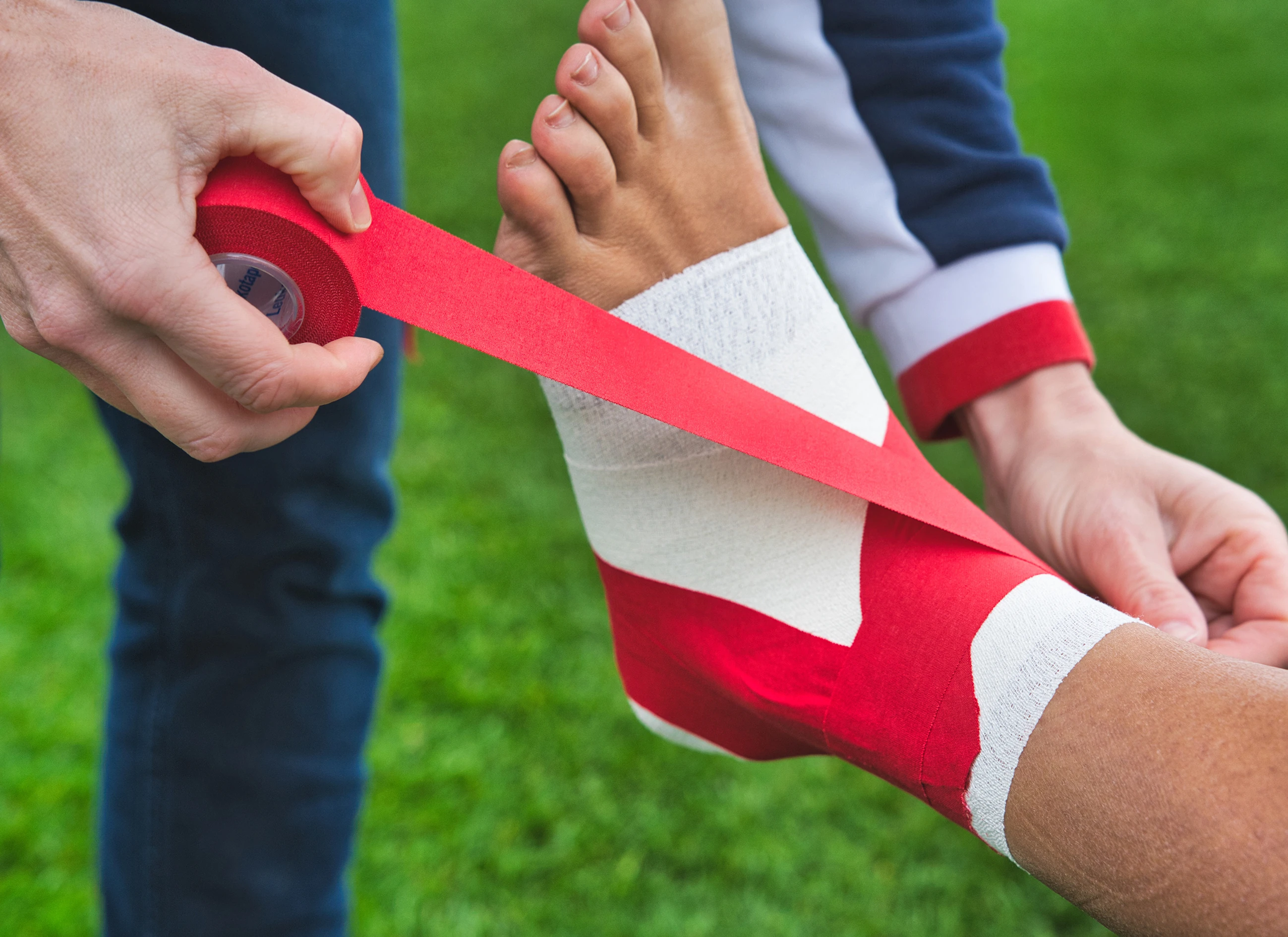 Application de la bande Leukotape Classic sur le pied d’un athlète pour un bandage de soutien en extérieur.